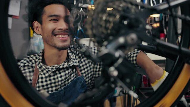 Happy Asian repairman smiling complacent while wearing chain of bike successful. Young man fixing and maintenance bike wheel in bicycle shop. Maintenance and repair Concept