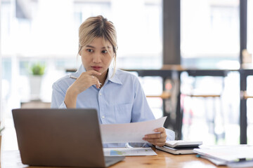Obraz premium Asian Business woman using calculator and laptop for doing math finance on an office desk, tax, report, accounting, statistics, and analytical research concept 