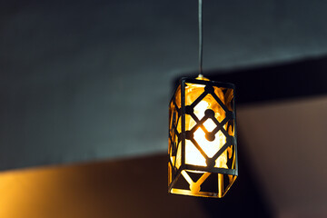 Fototapeta na wymiar A lamp with a rectangular iron frame suspended from the ceiling, illuminating in gold. Interior concept.