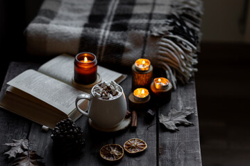 Aromatherapy on a grey fall morning, atmosphere of cosiness and relax. Autumn cozy home composition with hot chocolate with marshmallow and candles. Wooden background, books, close up.