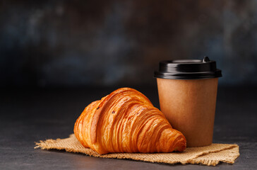 Aromatic coffee in a paper cup paired with a flaky croissant