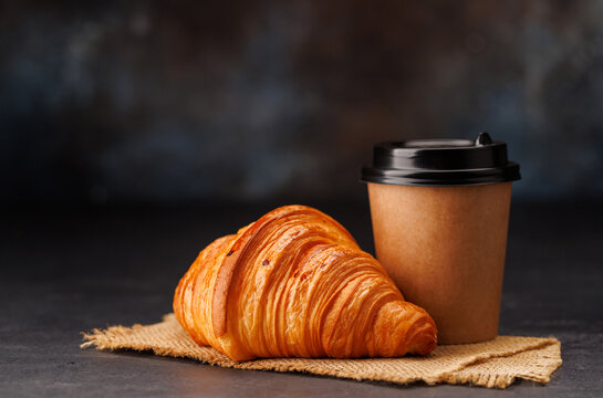 Aromatic coffee in a paper cup paired with a flaky croissant