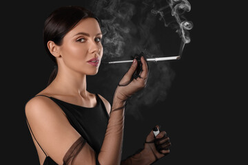Obraz premium Woman using long cigarette holder for smoking on black background, space for text