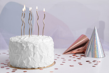 Delicious cake with burning candles and party hats on white table. Space for text