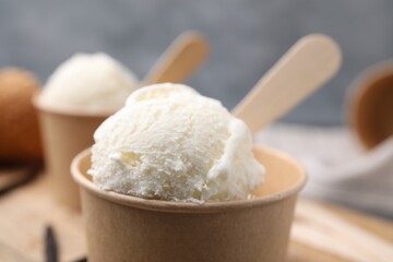 Paper cups with delicious ice cream and vanilla pods on wooden board, closeup