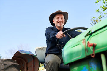 Mature farmer driving green tractor on sunny day