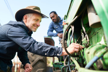 Farmer repairing engine while colleague sitting on tractor
