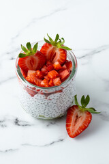 Vegan chia seeds pudding with coconut milk and strawberry. Healthy breakfast. Raw food and dieting concept. Summer dessert on the marble background. Portioned dessert in the glass jar