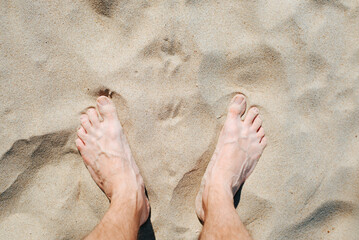 Barefoot caucasian male feet on sand on sunny summer day, top view