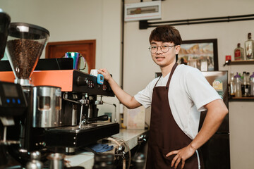 Portrait smiling Asian man barista in white t-shirt and apron standing at coffee shop. SME business coffee shop concept.