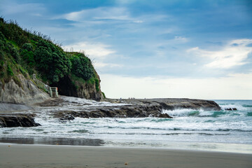 Sunset at Muriwai beach with waves splashing against the rocks and fishermen silhouettes in the distance. Auckland, New Zealand