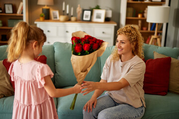 Daughter congratulating her mother and giving her bouquet of flowers at home