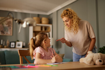 Mother scolding her daughter while helping her with homework at home