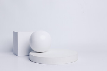 Modern set from various geometric shapes of white cube on cylinder pedestal podium, sphere and white stones decorated on white background. Stylish background for product presentation