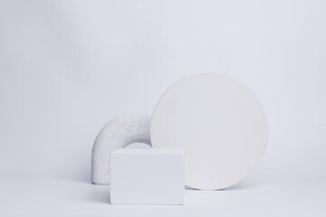Modern set from various geometric shapes of white cube on cylinder pedestal podium, sphere and white stones decorated on white background. Stylish background for product presentation