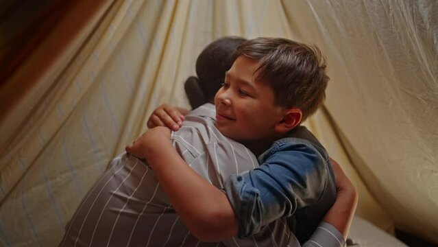 Close-up ethnic mother and son hugging, wishing good night before going to bed, inside a play tent