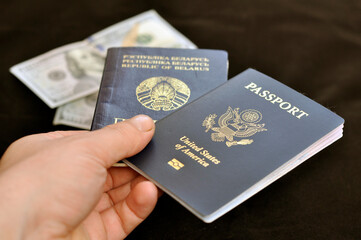 A hand with a passport of a citizen of the USA and Belarus against the background of US dollar banknotes. Emigration. Identification.