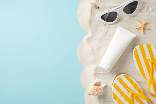 UV protection and summer essentials theme. Top view of sunblock cream without branding, accompanied by glasses, flip-flops, seashells, starfish on pastel blue and sandy background with space for label