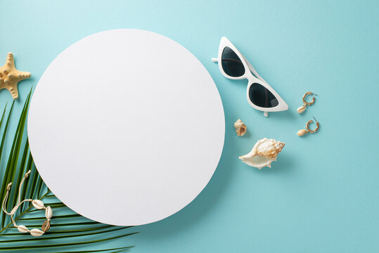 Visual delight of beach weekend essentials: trendy sunglasses, a fashionable shell earrings and bracelet, starfish, tropical palm leaf. Serene pastel blue backdrop with vacant circle for text or ad