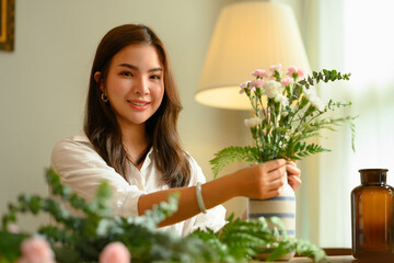 Attractive young female creating beautiful bouquet with different flowers, enjoying arranging flowers as a hobby at home