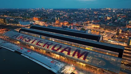 Schilderijen op glas Aerial view of famous places Amsterdam, Netherlands. View of canal and old centre district. railway station Amsterdam Centraal view at night © Dmytro Kosmenko