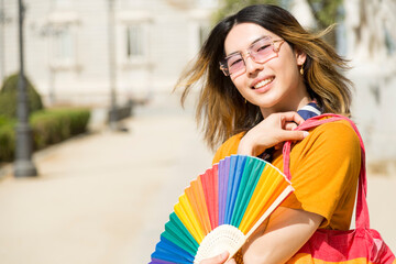Young non-binary person with pride fan looking at the camera on a sunny day