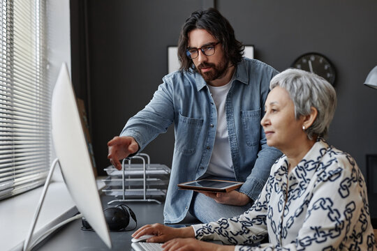 Side view portrait of senior woman using computer in class with male teacher helping, copy space