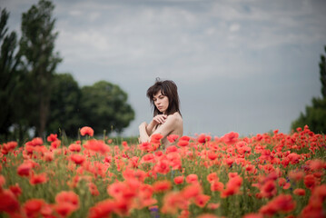Obraz na płótnie Canvas A girl with black hair and bare shoulders poses in a poppy field.