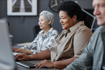 Side view portrait of senior black woman using computer and smiling in school for elderly people,...