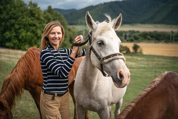 Fototapeta premium Young woman cleaning white gray horse with brush, her head next to animal
