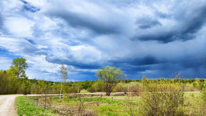 Dark, stormy and rainy clouds over green trees and big field on a spring or summer day