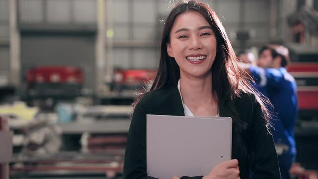 Successful woman standing and hugging document file looking at camera smiling have confidence in warehouse at factory. Pride and accomplishment concept.