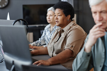Side view portrait of mature black woman using computer in programming class for seniors