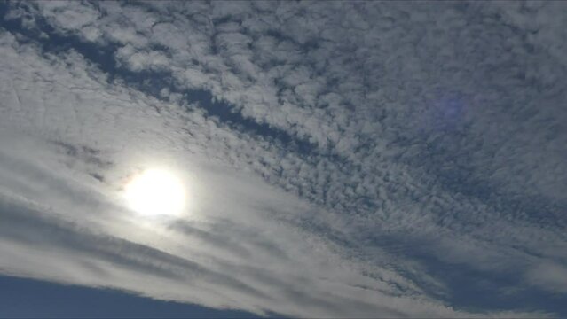 Natural blue sky background with decorative Altocumulus clouds moving and Cloud iridescence, irisation around sun - time lapse. Clouds with colorful pearl colors in clouds texture - optical phenomenon