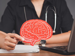 Brain Health and dementia. Doctor holding a red brain symbol while sitting at the table in the...