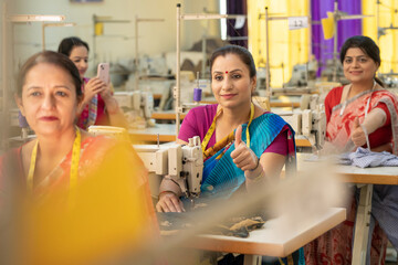 Indian woman showing thumbs up while work on sewing machine at textile factory.