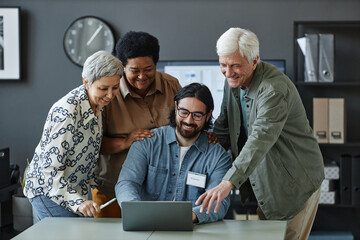 Diverse group of smiling senior people using laptop with man explaining technology in computer class