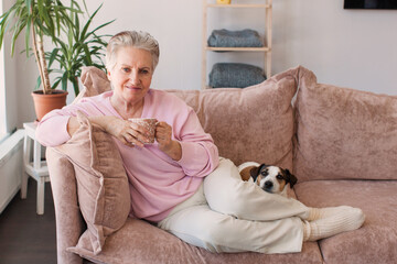 mature older adult grey-haired woman drinking coffee relaxing on sofa at home