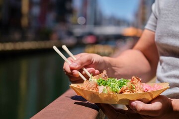 Unrecognizable man eating takoyaki at Dotonbori canal in Osaka, Japan.