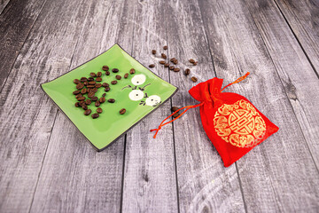 Coffee beans on a green saucer with a red pouch next to it, wooden background, photo at an angle