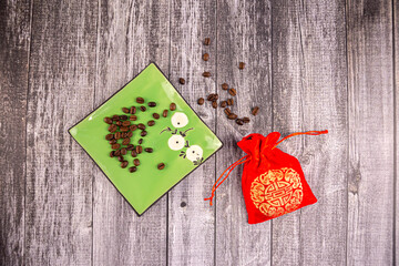 Coffee beans on a green saucer with a red bag next to it, wooden background, photo from above