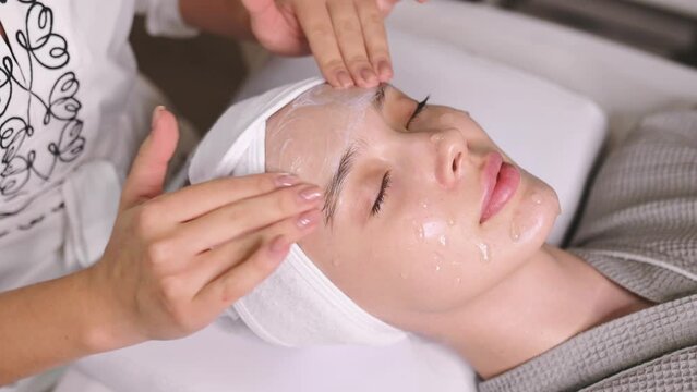 Spa day. Facial skin care procedures in a beauty salon. The cosmetologist applies a special cream, scrub, peeling to the face of a pretty caucasian woman to improve the quality of facial skin