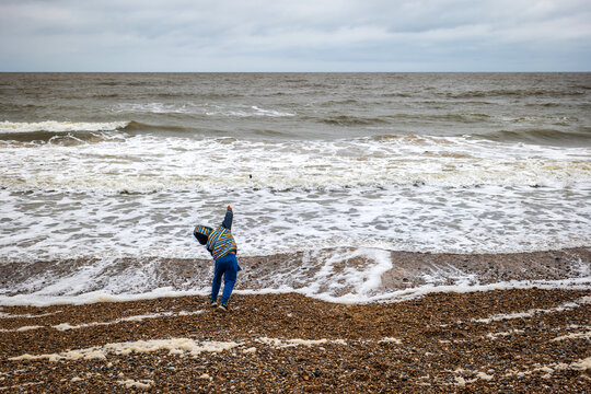 child boy throwing stone into the sea in england uk