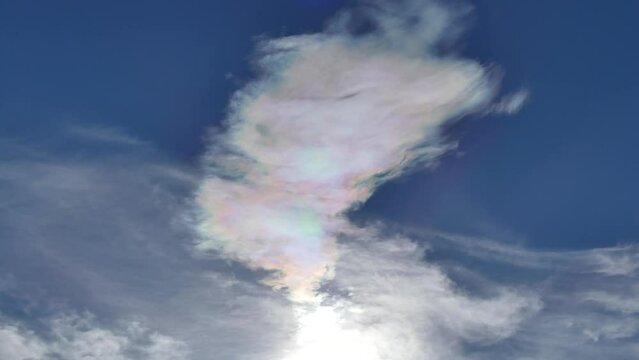 Natural blue sky background with different types of clouds moving very slowly and Cloud iridescence, irisation around sun. Sunny autumn calm sky with colorful pearl colors - optical phenomenon.