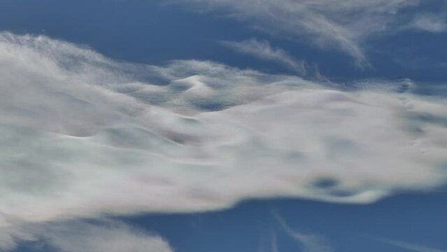 Natural blue sky background with Cloud iridescence, irisation around sun moving very slowly in shape of waves. Sunny autumn calm sky with colorful pearl colors - optical phenomenon in clouds.
