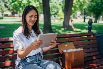 Young Japanesse woman using digital tablet while resting in the park