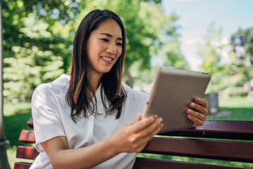 Young Japanesse woman using digital tablet while resting in the park