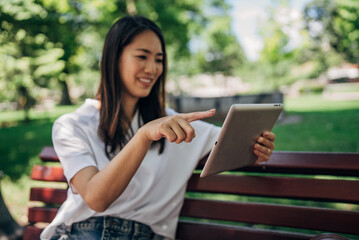 Fototapeta premium Young Japanesse woman using digital tablet while resting in the park