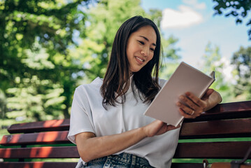 Fototapeta premium Young Japanesse woman using digital tablet while resting in the park