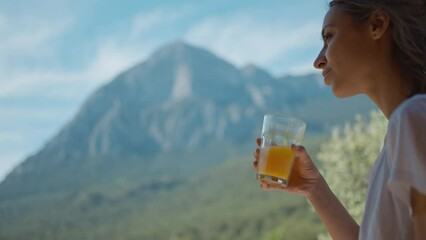 happy mixed race woman at sunny morning outdoors in mountain camping enjoying sunrise and drinking fresh orange juice. traveling, wellbeing and healthy nutrition concept. muontains ridge on background - Powered by Adobe